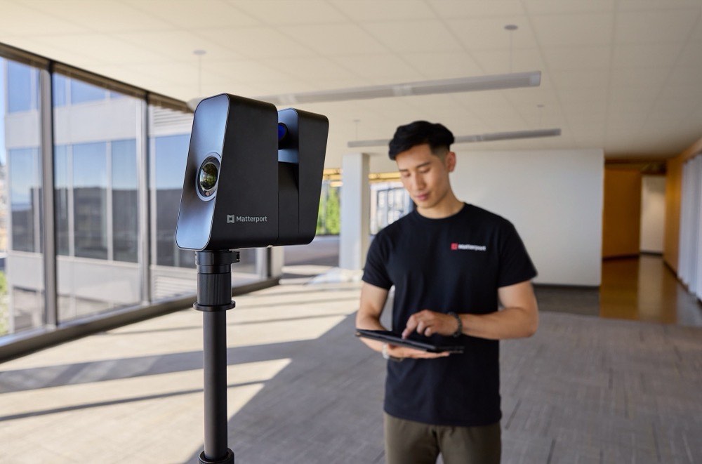 Matterport-Kamera auf einem Stativ in einem hellen Innenraum, eine Person prüft die Aufnahme auf einem Tablet